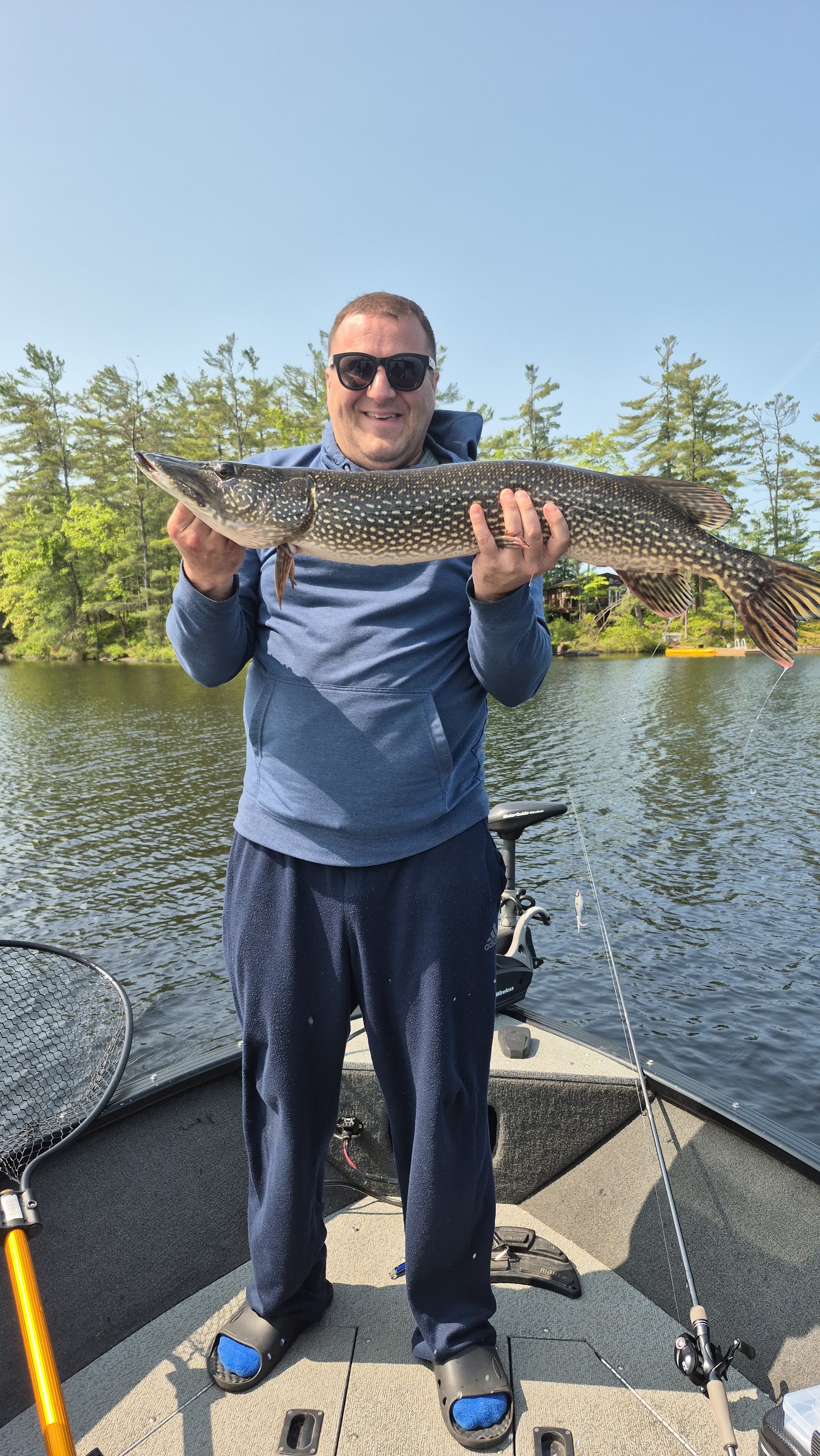 Man holding a large fish by a lake with a boat in the background